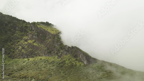 A video green mountain ridge, covered in vibrant vegetation, with fluffy clouds drifting across it