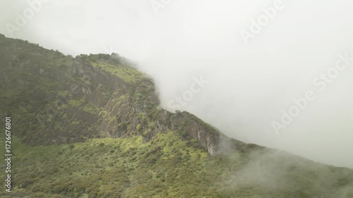 A video green mountain ridge, covered in vibrant vegetation, with fluffy clouds drifting across it