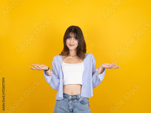 Woman spreading hands aside, portrait of young caucasian 20s trendy cute woman spreading hands aside smiling looking camera isolated on yellow studio background. Wear white top and shirt. Copy space.
