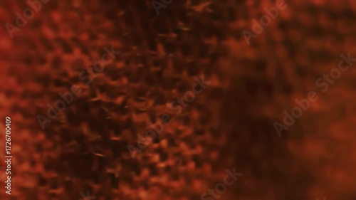 A beautiful abstract macro video of a warm red and orange woven fabric texture with a soft focus and gentle light movement creating a shimmering and glowing background loop.