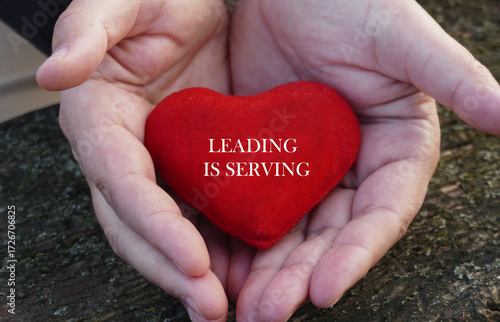 Leading is serving - man hold in hands a red heart with motivational text
