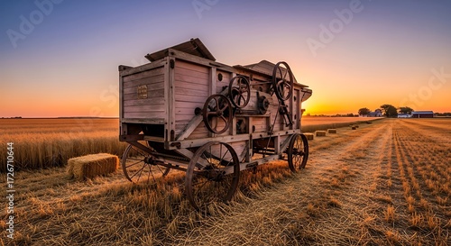 Vintage farm thresher machine in golden wheat field at sunset