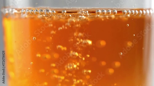 A mesmerizing extreme closeup macro video of golden amber beer or cider with effervescent bubbles rising to form a crisp white foam head in a clear glass.