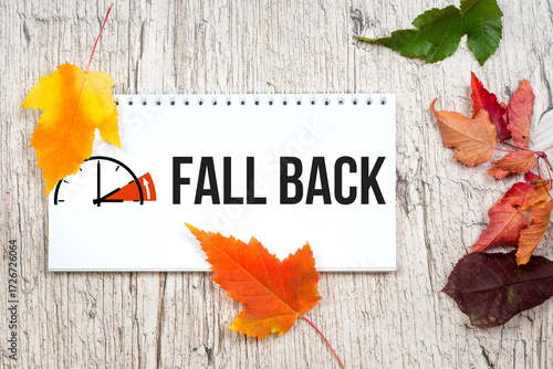 fall back 1 hour, autumn colorful leaves and blank horizontal notepad on light wooden table