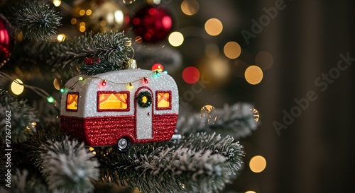 Glittery camper travel trailer Christmas ornament on a frosted pine tree branch with bokeh lights