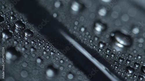 Extreme close up macro shot of water droplets condensing and flowing on a dark metallic hydrophobic surface creating a beautiful abstract background with shallow depth of field.
