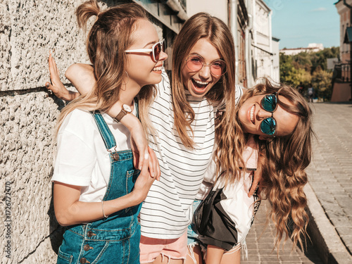 Portrait of three young beautiful smiling hipster female in trendy summer clothes. Sexy carefree women posing on the street background.Positive models having fun in sunglasses.Hugging