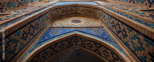 Ornate Islamic architecture with blue mosaic tile work and detailed geometric patterns on a brick facade, photographed from below within the historical necropolis complex in Samarkand, Uzbekistan.