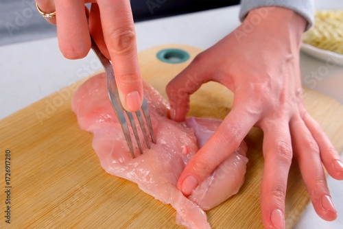 Skilled female chef woman hands cooking piercing raw chicken breast with fork on cutting board. Culinary preparation technique for meal cooking process. Cuisine recipe domestic healthy poultry food.