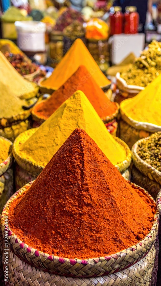 Fototapeta premium Colorful spice piles in woven baskets. A vibrant array of conical piles of different colored spices, likely turmeric and paprika, are showcased in tightly arranged woven baskets. 