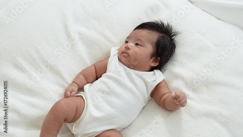 Asian newborn baby girls wearing a white bodysuit laying on the bed.