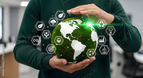 Person holding a green earth globe with environmental icons floating around it in a blurred office