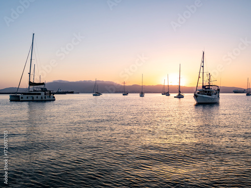 Yachts and sailboats moored in Gibraltar Bay at dusk, with silhouettes reflecting in calm waters against a glowing Mediterranean sunset.