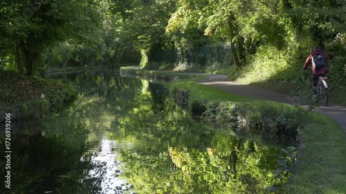 Cyclist Riding Along Tree-Lined Canal Towpath in Birmingham, UK.
A cyclist rides along the towpath of the Birmingham to Worcester Canal near Birmingham University.