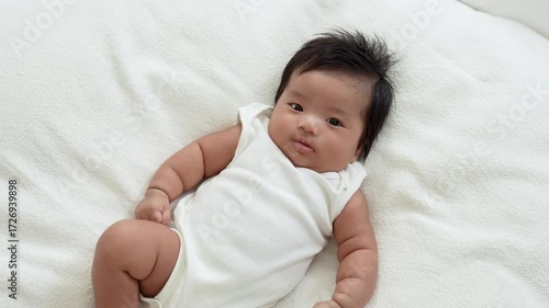 Asian newborn baby girls wearing a white bodysuit laying on the bed.