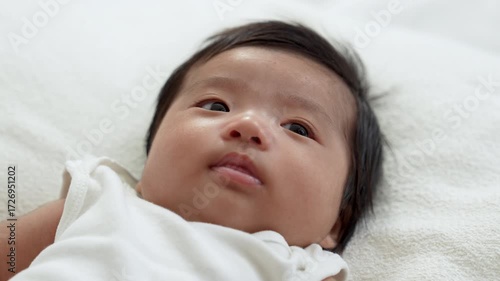 Asian newborn baby girls wearing a white bodysuit laying on the bed.