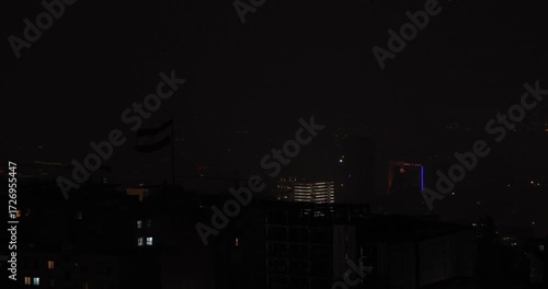 Wallpaper Mural Tehran city skyline at night with Iranian flag visible in the foreground. Lightning from a thunderstorm illuminates the hazy sky, creating a dramatic and cinematic urban night atmosphere. Torontodigital.ca