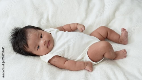 Asian newborn baby girls wearing a white bodysuit laying on the bed.