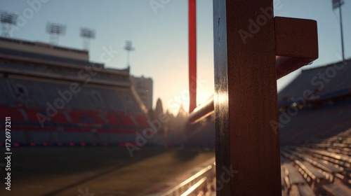 Football goalpost on empty stadium field under dramatic sunset lighting.