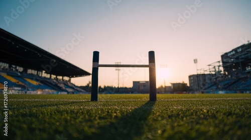 Football goalpost on empty stadium field under dramatic sunset lighting.