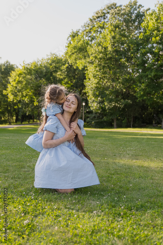 Valokuva Daughter hugs and kisses her mother in the sunlight, wearing blue dresses