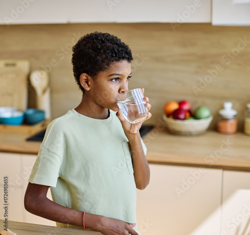 Fotografía Portrait of a child, teen black boy,  drinks fresh Water in the Kitchen, holds a