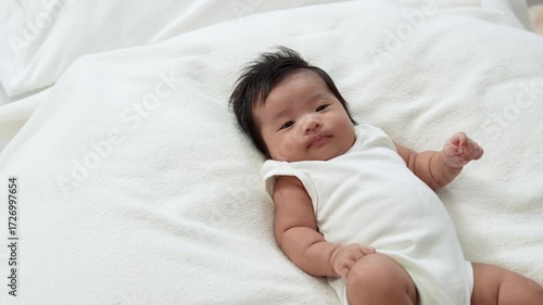 Asian newborn baby girls wearing a white bodysuit laying on the bed.