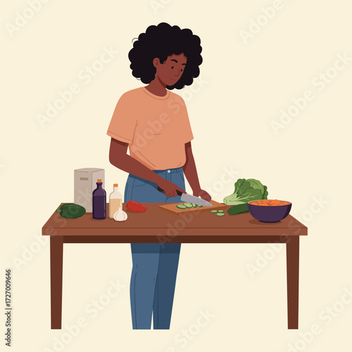 A young Black woman with curly hair chopping vegetables on a wooden table in her kitchen, preparing a healthy meal.
