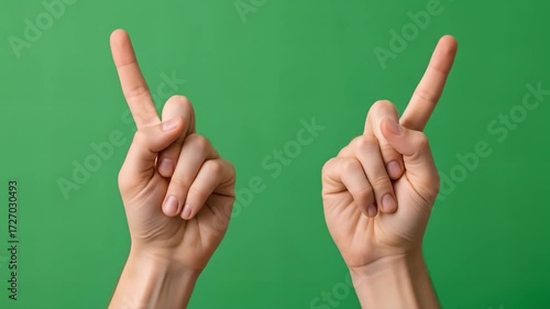 Two hands making the peace sign with index fingers pointing upwards against a green background.