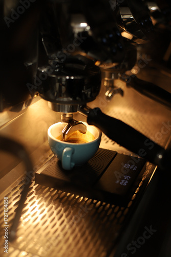 A barista makes a cappuccino with beautiful latte art against the backdrop of a coffee machine with bright background lighting.