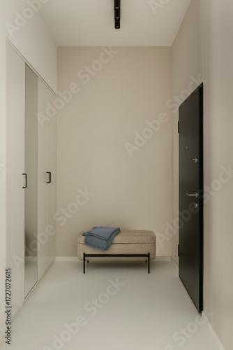 Minimalist hallway with black door, beige walls, upholstered bench and folded blue throw.