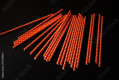 Bright orange paper straws with white polka dots arranged on a dark surface, perfect for parties and celebrations