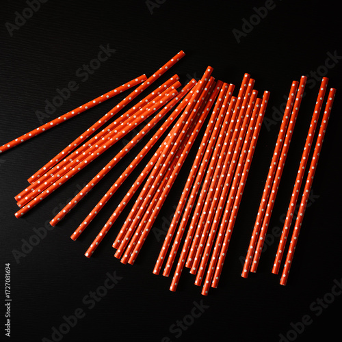 Collection of bright orange paper straws scattered on a dark surface highlighting festive design and playful patterns