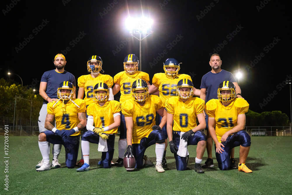 Fototapeta premium American football team and coaches standing and kneeling, posing on a green field at night