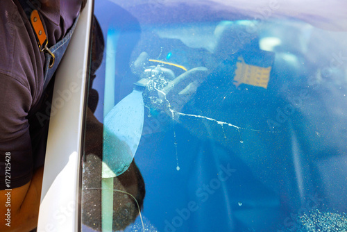 Broken car windshield with spider web crack pattern glass shows impact damage with specialist works on fixing crack in car windshield using repair tool