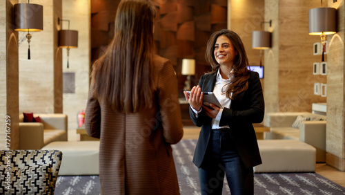 Hotel staff member welcoming guest, offering professional service and hospitality with tablet during check-in