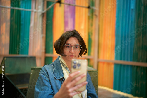 Woman with glasses holding a smartphone in a colorful, vibrant indoor setting. Brussels, Belgium