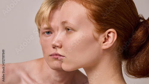 Quadro em tela Close side profile of red-haired woman with blond man blurred behind on neutral background