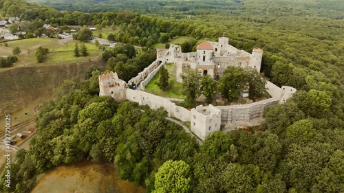 Aerial drone footage circling Tenczyn Castle in Poland, showcasing the medieval fortress from all angles. The view highlights the stone walls, towers, and surrounding scenic landscapes.