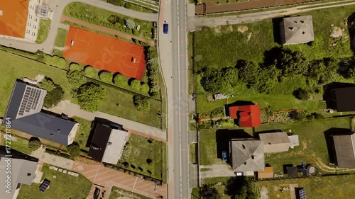 Aerial drone footage of a Polish village in summer, captured from a strict top-down perspective. The scene highlights rooftops, streets, and the colorful layout of the settlement.