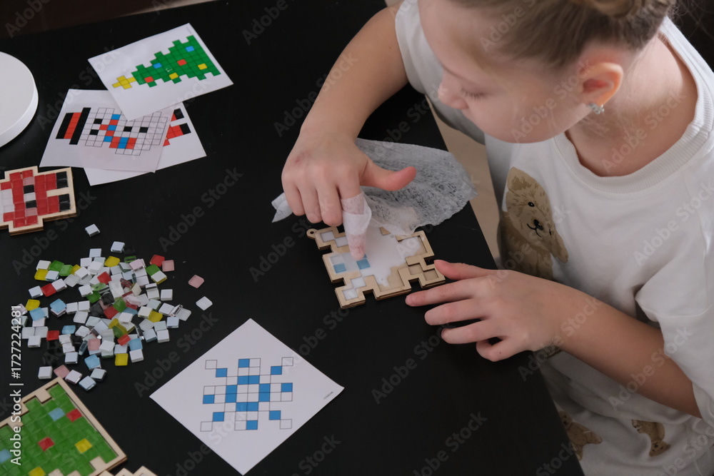 Obraz premium A girl makes a Christmas toy with her own hands from ceramic mosaic. Ceramic mosaic, DIY Christmas tree toy. Eco-friendly toy, educational activity for children.