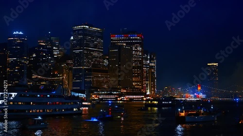 Diverse boats stand on the dark waterscape watching night firework show. View on the beautiful high-rise building at the skyline of New York, USA.