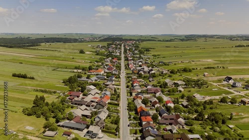 A breathtaking wide aerial view of Suloszowa village in Poland, capturing its long main street, surrounding fields, and colorful rural landscape under a clear sky.