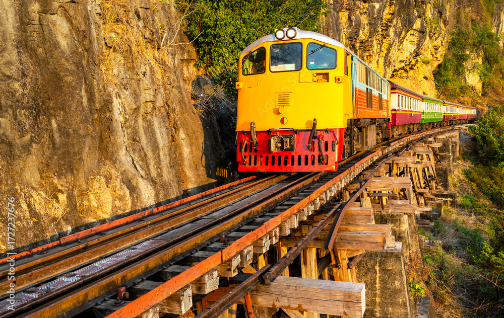 Fototapeta premium Train running across Thai-Burma Death Railway,at Tham Krasae Bridge,alongside the River Kwai,Kanchanaburi,Thailand.
