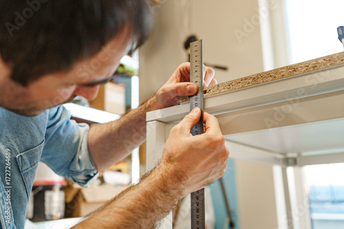 Person measuring wooden furniture piece during DIY carpentry project indoors