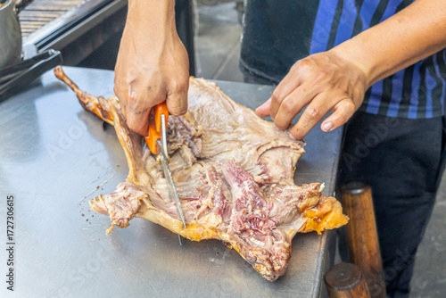 Person cutting roasted guinea pig with kitchen scissors on a metal table, a typical Andean dish from Ecuador. Traditional gastronomic scene reflecting culture and authentic flavors of the Andes.