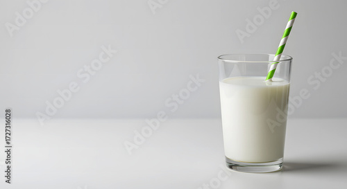 Glass of milk with green straw on white background for St. Patrick's Day  