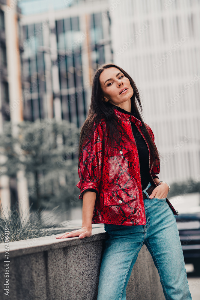 Fototapeta premium Chic urban woman in stylish red jacket enjoying outdoor lifestyle in a modern city setting, vertical photo