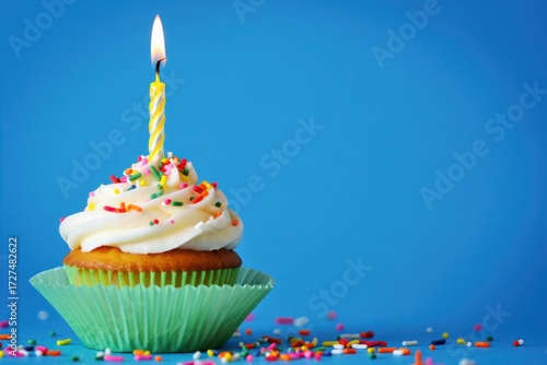 Single cupcake with white frosting and colorful sprinkles topped with a lit birthday candle image