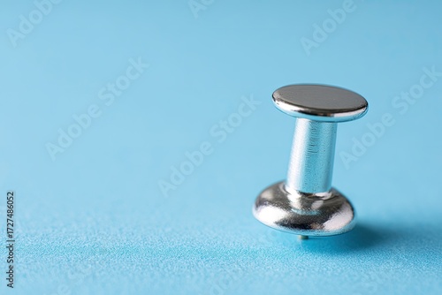 Close-up of a silver push pin on a light blue background